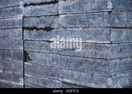 Close-up side view of stacked polished grey granite slab tiles with a geometric pattern prepared for building facade or paving construction. Stock Photo