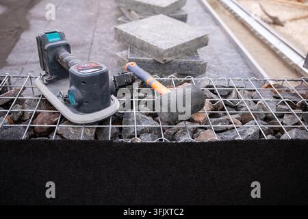 Professional tile installation tools including a suction cup vibrator and rubber mallet placed on a gabion wall at an outdoor hardscaping construction Stock Photo