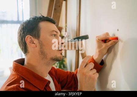 Man installing an orange plastic wall plug into a drilled hole, holding a hammer in the other hand, focusing on completing a home renovation or repair task Stock Photo