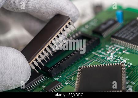 A technician works on a circuit board, carefully placing a chip in its socket in a repair shop during daylight hours. Stock Photo
