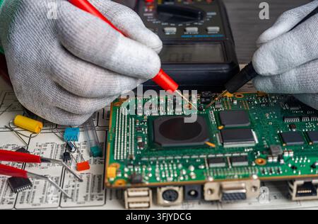 Workers conduct quality control and repair on a circuit board in a manufacturing area while using tools and testing equipment. Stock Photo