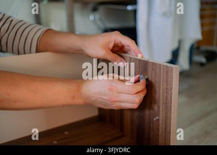 Person's hands meticulously assembling a wooden flat pack tv stand, inserting a cam lock into a pre drilled hole, demonstrating the process of home improvement and furniture construction Stock Photo