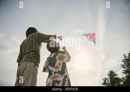 Father and Child Flying Colorful Kite Outdoors on Sunny Day Stock Photo