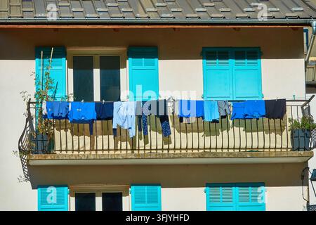 Sunlit Balcony Laundry With Blue Clothes Hanging on Clothesline Under Turquoise Shutters Stock Photo