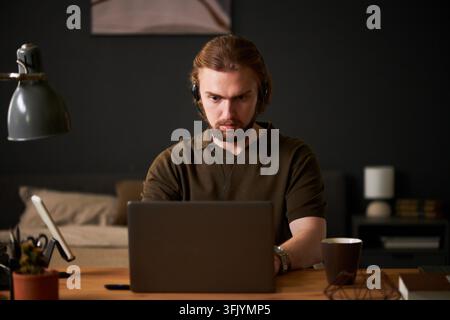 Focused Man with Headphones Working on Laptop at Home Stock Photo