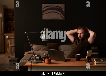 Man Taking Break from Working on Laptop at Home Desk at Night Stock Photo
