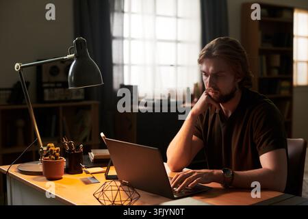 Focused Man Working on Laptop at Night Desk at Home Stock Photo
