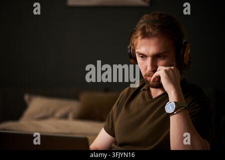 Focused Man in Headphones Working on Laptop at Home in Evening Stock Photo
