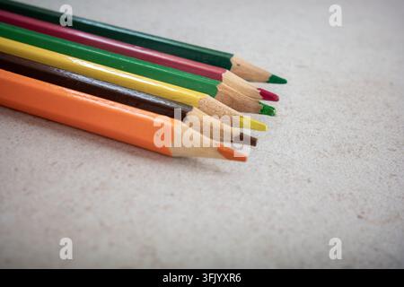 Several colored pencils are laid out on a plain surface. They are in a line and show various colors. This setup is suitable for drawing or coloring pr Stock Photo