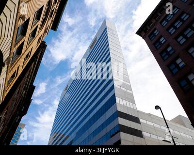 Low-angle worm's-eye view of a contemporary glass and steel skyscraper rising between older brick buildings in downtown Cincinnati. Stock Photo
