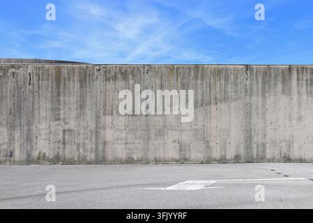 Dirty weathered reinforced concrete  wall with blue sky and clouds above. Street in front with directional arrow painted. Background for copy space. Stock Photo