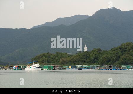 Fishing rafts and boats dock in Sam Mun Tsai, Hong Kong, for aquaculture, beneath the towering Guanyin statue at Tsz Shan Monastery. Stock Photo