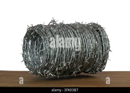 A coiled roll of barbed wire rests on a wooden table against a white background. Stock Photo