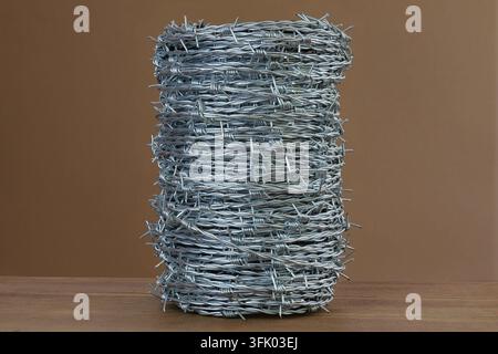 A coiled bundle of barbed wire stands on a wooden surface against a plain background. Stock Photo