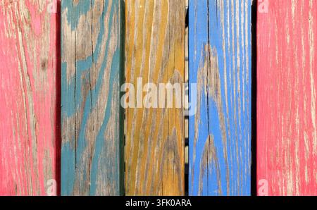Weathered wooden planks are arranged vertically, showcasing peeling paint in shades of pink, blue, and yellow, creating a vibrant textured background Stock Photo