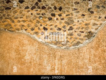 Old stone wall texture meeting an eroded plastered surface with a distinct wavy line Stock Photo