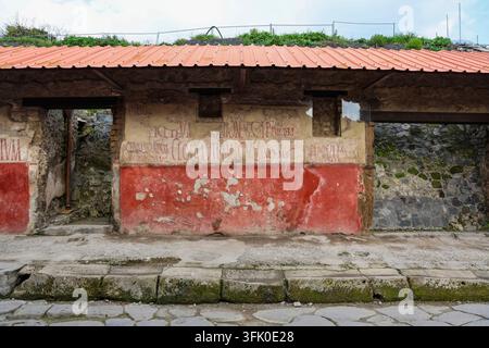 Pompeii, Italy 8. March 2026, Preserving ancient ruins with red frescoes and Latin inscriptions under a modern protective roof Stock Photo