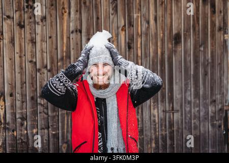 Snow covered man laughing in front of rustic wooden cabin during winter. Stock Photo