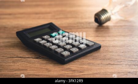 Black Digital Calculator Beside Clear Incandescent Light Bulb on Wooden Surface Concept for Utility Bill Calculation, Energy Cost Analysis, and Smart Stock Photo