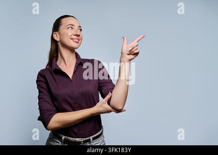 Smiling young woman pointing finger up at copy space against grey background Stock Photo