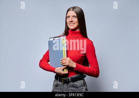 Smiling young woman holding notebook and clipboard looking at camera Stock Photo