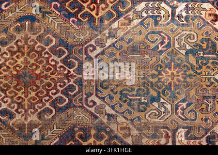 Closeup front view of an antique oriental carpet showing intricate geometric motifs, faded colors and worn texture. Decorative woven textile evokes vi Stock Photo