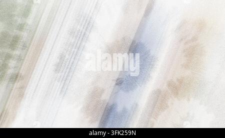 A close-up of a light-colored fabric with a gentle tie-dye pattern, featuring soft washes of blue and beige on a textured surface. Stock Photo