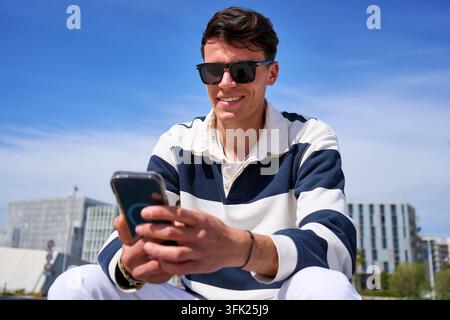 Young man smiling using smartphone in urban setting Stock Photo