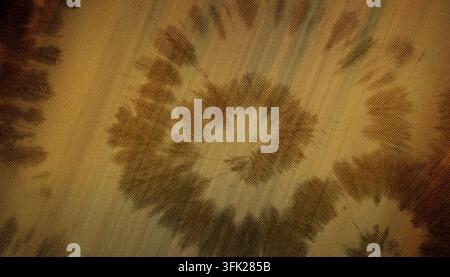 A close-up view of a golden yellow fabric featuring a swirling tie-dye pattern with a distinct linear texture throughout the material. Stock Photo