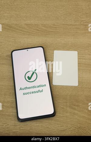 Smartphone screen displaying "Authentication successful" message with a green checkmark, placed on a wooden table beside a blank white digital access Stock Photo