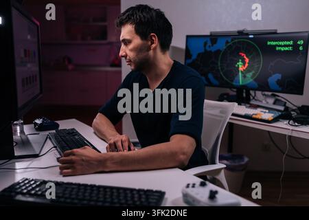 Concentrated man works at desk with multiple monitors in dark room. Screen glow illuminates face. Concept of cybersecurity, hacking, coding, remote Stock Photo