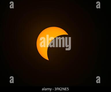 A brilliant orange solar crescent glows intensely against the vast darkness of a deep black sky during a partial eclipse. Stock Photo