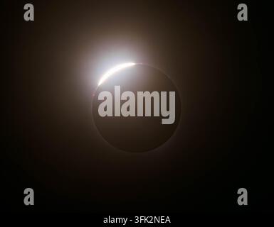 A bright flash of light pierces through the edge of a dark moon during a total solar eclipse in the night sky. Stock Photo