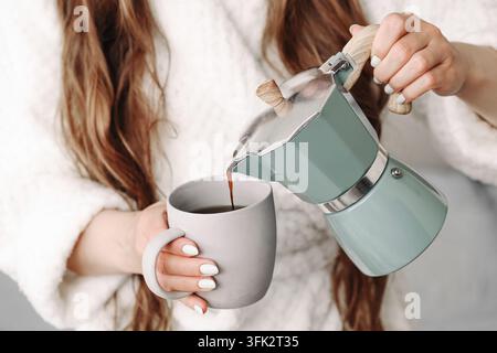 Woman pouring hot drink from moka pot into cup. Coffee background for home brewing morning beverage espresso preparation and daily breakfast routine. Stock Photo
