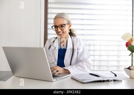 Smiling middle-age female doctor working on laptop Stock Photo