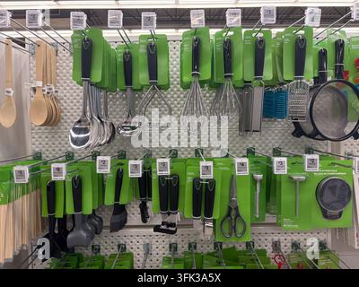 Retail store display featuring various kitchen utensils including ladles, whisks, and graters hanging on a pegboard wall. Stock Photo