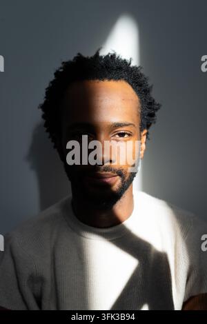 African American man posing with ribbed sweater against smooth gray wall with light bisecting face Stock Photo