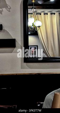 A gold-toned multi-globe branching wall sconce or pendant light reflected in a dark-framed mirror. Stock Photo