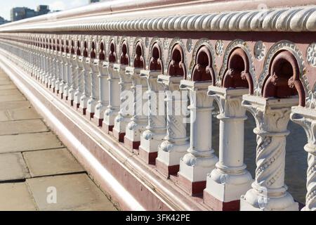 A close-up of the iconic red-and-white cast-iron balustrade on London's Blackfriars Bridge, a protective railing above the River Thames. Stock Photo