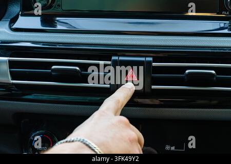 Close-up of a finger pressing the red hazard warning light button on a modern car dashboard panel Stock Photo