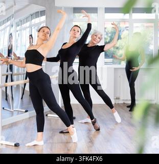 Middle-aged woman teacher conducts class, girls engaged in ballet studio, perform repetitions of elements and tasks, doing complex with Batman. Mentor Stock Photo