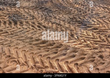 Deep rhythmic herringbone tractor tire tracks imprinted in damp textured soil, industrial agricultural marks left by heavy machinery on a rural field, Stock Photo