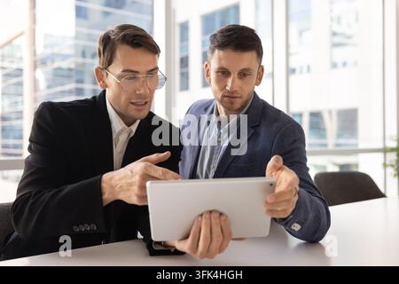 Focused male corporate professionals analyzing financial data on tablet screen Stock Photo