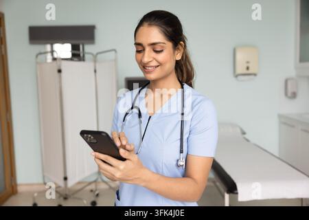 Smiling nurse using smartphone in exam room Stock Photo
