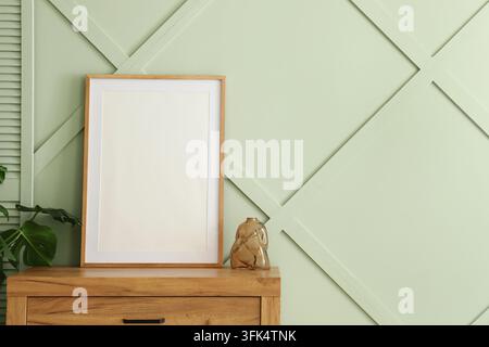 Interior design mockup, blank wooden picture frame on a modern sideboard with monstera plant and glass vase against a sage green wall background Stock Photo