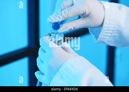 Medical research and pharmaceutical development, scientist pouring blue liquid into a glass beaker for chemical analysis in a modern laboratory settin Stock Photo