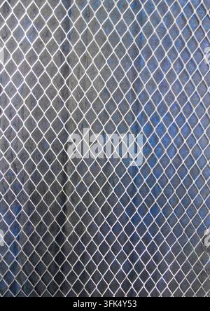 Metal mesh with diamond-shaped cells. Iron sheets partially covered with blue paint in the background Stock Photo