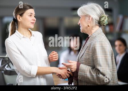 Adult woman and elderly woman greet each other with handshake in office space Stock Photo