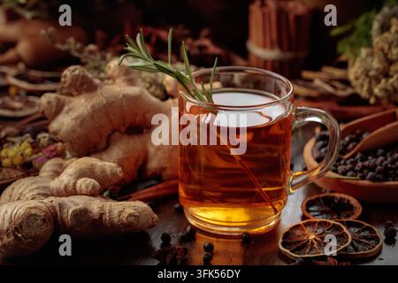 Warming herbal tea with fresh ginger, dried orange slices, juniper berries and spices served in a glass mug. Rustic composition with natural ingredien Stock Photo