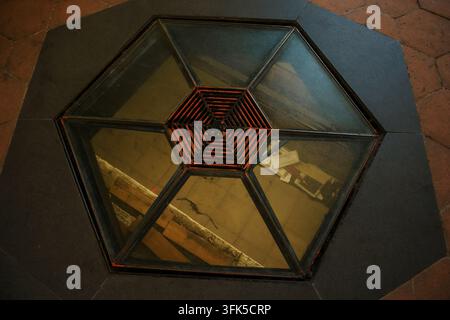 Hexagonal floor glass skylight at San Nicolo l'Arena Benedictine Monastery in Catania, Sicily, Italy, featuring a centered red metal grill, showing architectural structure and modern industrial design Stock Photo